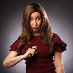 Promotional photo of Jane Japes, a white woman with long auburn hair in a red dress. She is holding a microphone and making a silly face with her tongue sticking out.