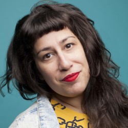 Promotional photo of Eve Ellenbogen, a white woman with long wavy dark hair, red lipstick and a yellow shirt. Her head is tilted to the side and she has a quizzical look on her face. The background is teal.