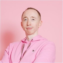 Promotional photo of Patrick Susmilch, a white man with cropped hair in a pink shirt against a pink background.